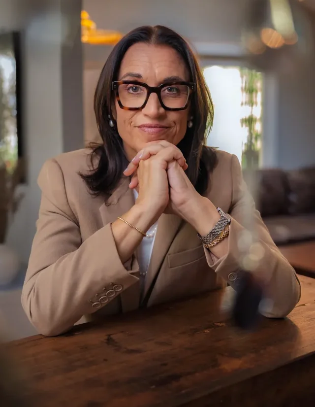 Woman in tortoiseshell glasses resting her chin on her hands at a wooden table