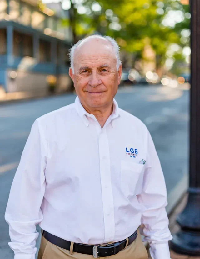 Older man in a white company shirt on a tree-lined main street