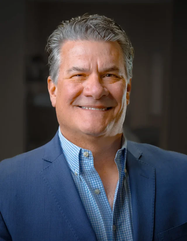 Smiling man in a blue blazer and gingham shirt, studio headshot